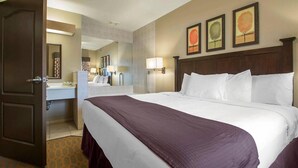 A hotel room with a large bed, a bedside table, a mirror, and a wall with three framed pictures. - Wisconsin Dells Family Stay with Water Park Access & Spacious 2BR Suite (Wisconsin Dells)