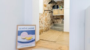 Een trap met houten treden en een mat, die leidt naar een keuken met stenen muren en een hangende kruidenrek.