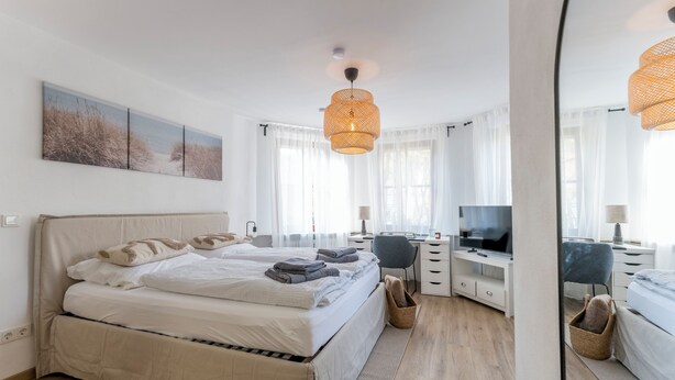 Een slaapkamer met een bed, een bureau, een stoel, een televisie en een grote spiegel.