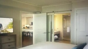 A bedroom with a bed, a ceiling fan, and a TV on a dresser. There is a door leading to a bathroom and a kitchen area. - Ocean Front View Hilton Head Island 2 bedroom Condo sleeps 8 w/ Golf access (Hilton Head Island)