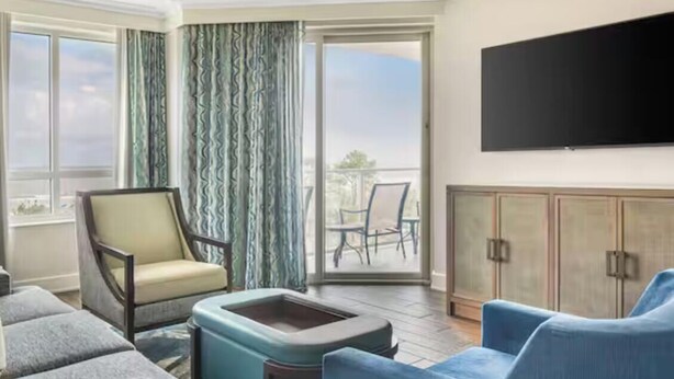 A hotel room with a balcony, a flat-screen TV, a sofa, a chair, and a cabinet. - Ocean Front View Hilton Head Island 2 bedroom Condo sleeps 8 w/ Golf access (Hilton Head Island)