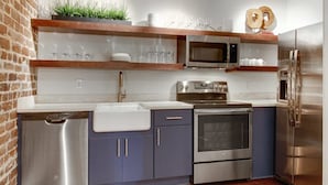 A modern kitchen with stainless steel appliances, wooden shelves, and a brick wall. - 10BR Downtown Savannah Combo | Walk to Nightlife (Savannah)