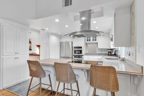 A modern kitchen with white cabinets, stainless steel appliances, and a central island with bar stools. - San Diego Hidden Gem: 4BR w/ Spa + Putting Green (San Diego)