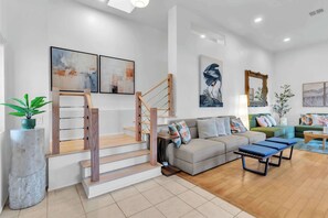 A modern living room with a staircase, a sofa, a coffee table, and artwork on the walls. - San Diego Hidden Gem: 4BR w/ Spa + Putting Green (San Diego)