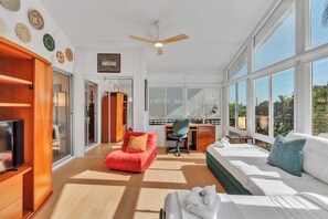 A modern hotel room with a large window, a desk, a red chair, a white sofa, and a television. - San Diego Hidden Gem: 4BR w/ Spa + Putting Green (San Diego)