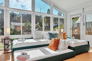 A spacious room with large windows, a bed with multiple pillows, a bedside table, and a lamp. - San Diego Hidden Gem: 4BR w/ Spa + Putting Green (San Diego)