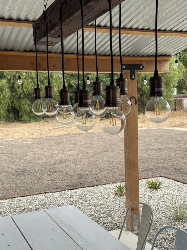 A covered outdoor seating area with a table and chairs, surrounded by a gravel path and greenery. - Welcome to the Red Barn House: 3BR 2BA country living in Santa Ynez Valley (Santa Ynez)