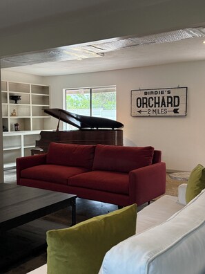 Ein Wohnzimmer mit einem roten Sofa, einem weißen Sofa, einem Klavier und einem Schild mit der Aufschrift 'Birdie's Orchard 2 miles'.