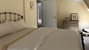 Ein Schlafzimmer mit einem großen Bett, einem Schminktisch, einer Tür und einem kleinen Tisch mit einem Bild.