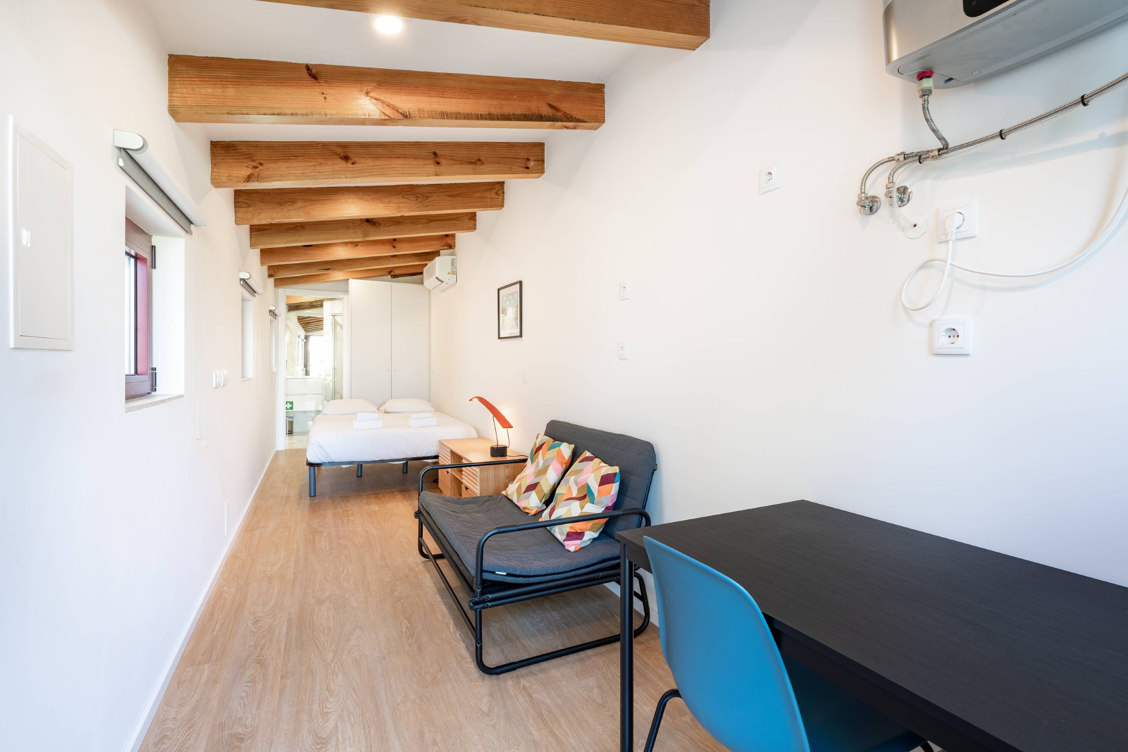 A modern room with exposed wooden beams, a bed, a desk, and a chair.