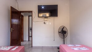 A room with two beds, a TV, a fan, and a door leading to another room. - Apto Para 5 Pessoas com Garagem e Churrasqueira (Para de Minas)
