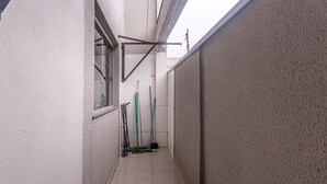 A narrow corridor with tiled flooring, a window on the left, and cleaning equipment against the wall. - Apto Para 5 Pessoas com Garagem e Churrasqueira (Para de Minas)
