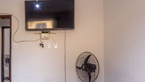 A television mounted on the wall, a standing fan, and a door leading to another room. - Apto Para 5 Pessoas com Garagem e Churrasqueira (Para de Minas)