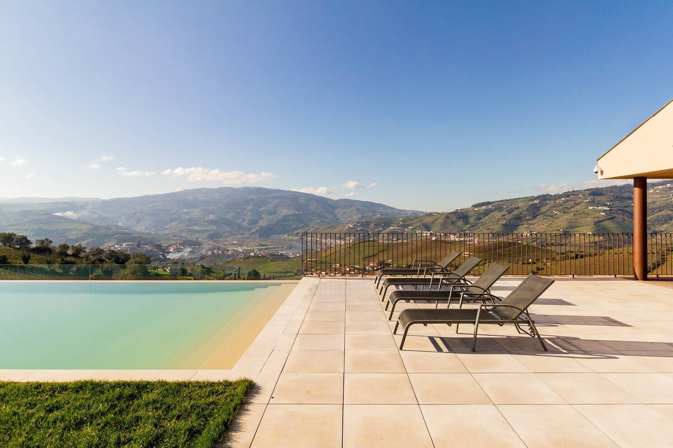 Ein Poolbereich mit Liegestühlen, einer gefliesten Terrasse und Blick auf ferne Berge.