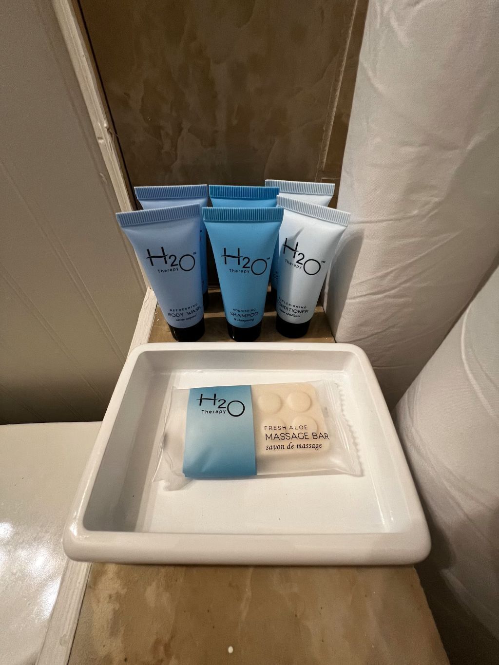 Ein Badezimmerschrank mit H2O Therapy Produkten, darunter Duschgel, Shampoo, Spülung und ein frischer Massage-Riegel mit Aloe Vera.
