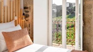 Une chambre à coucher avec un lit, une tête de lit en bois, une table de chevet, une lampe et une vue sur un balcon agrémenté de verdure.