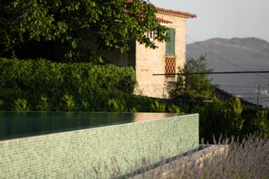 Una piscina con bordo piastrellato, un edificio in pietra con una finestra verde e una montagna sullo sfondo.