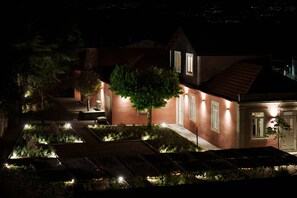 A house with a sloped roof, a tree in the yard, and a well-lit pathway.