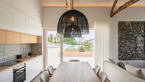 A modern kitchen with a dining area, wooden cabinets, a stone wall, and a view of a pool.