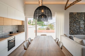 Una cucina moderna con zona pranzo, mobili in legno, parete in pietra e vista su una piscina.