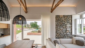 A modern kitchen with a wooden table and chairs, a stone wall, and a view of a pool and greenery.