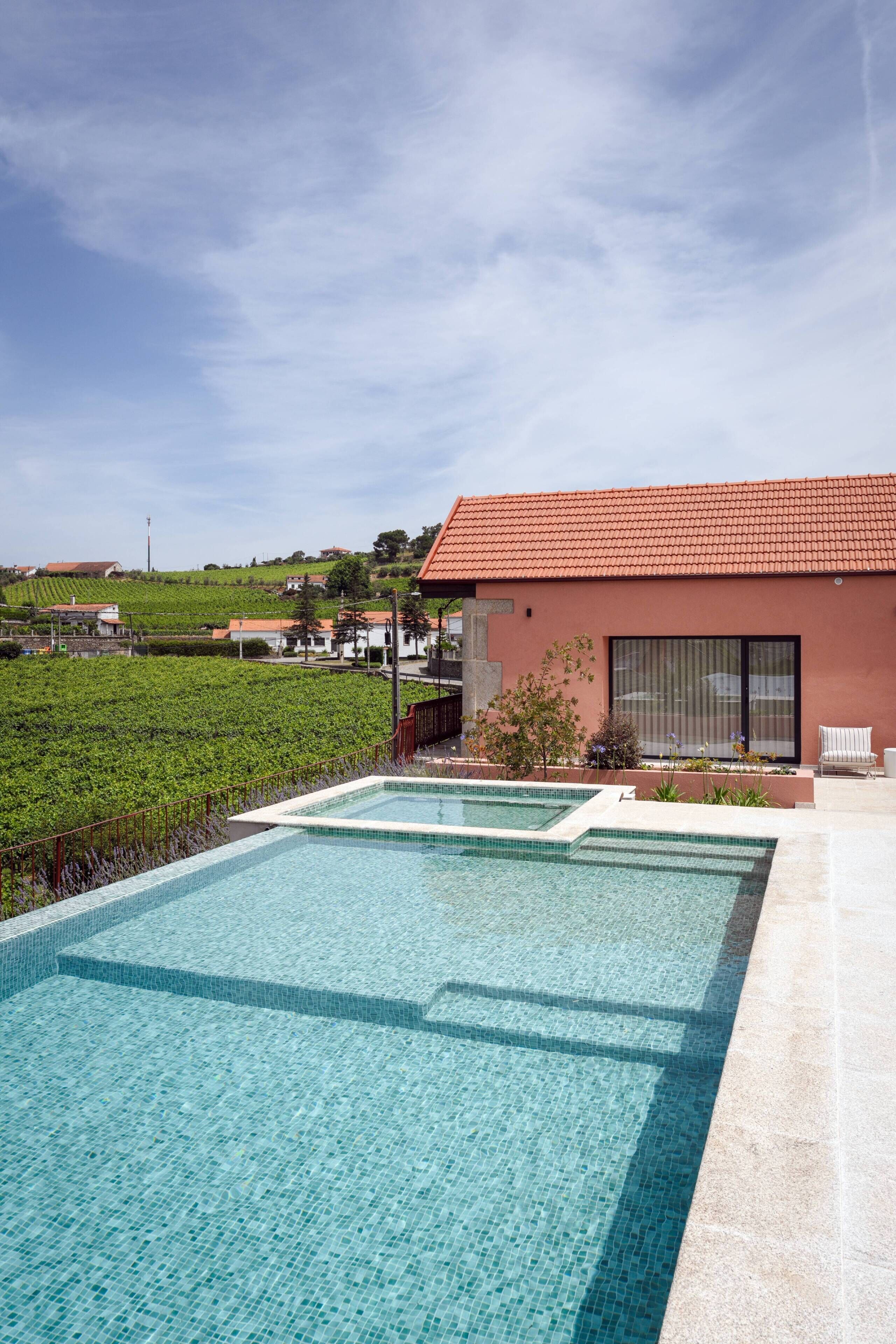A modern building with a swimming pool, a patio area, and a view of a vineyard.