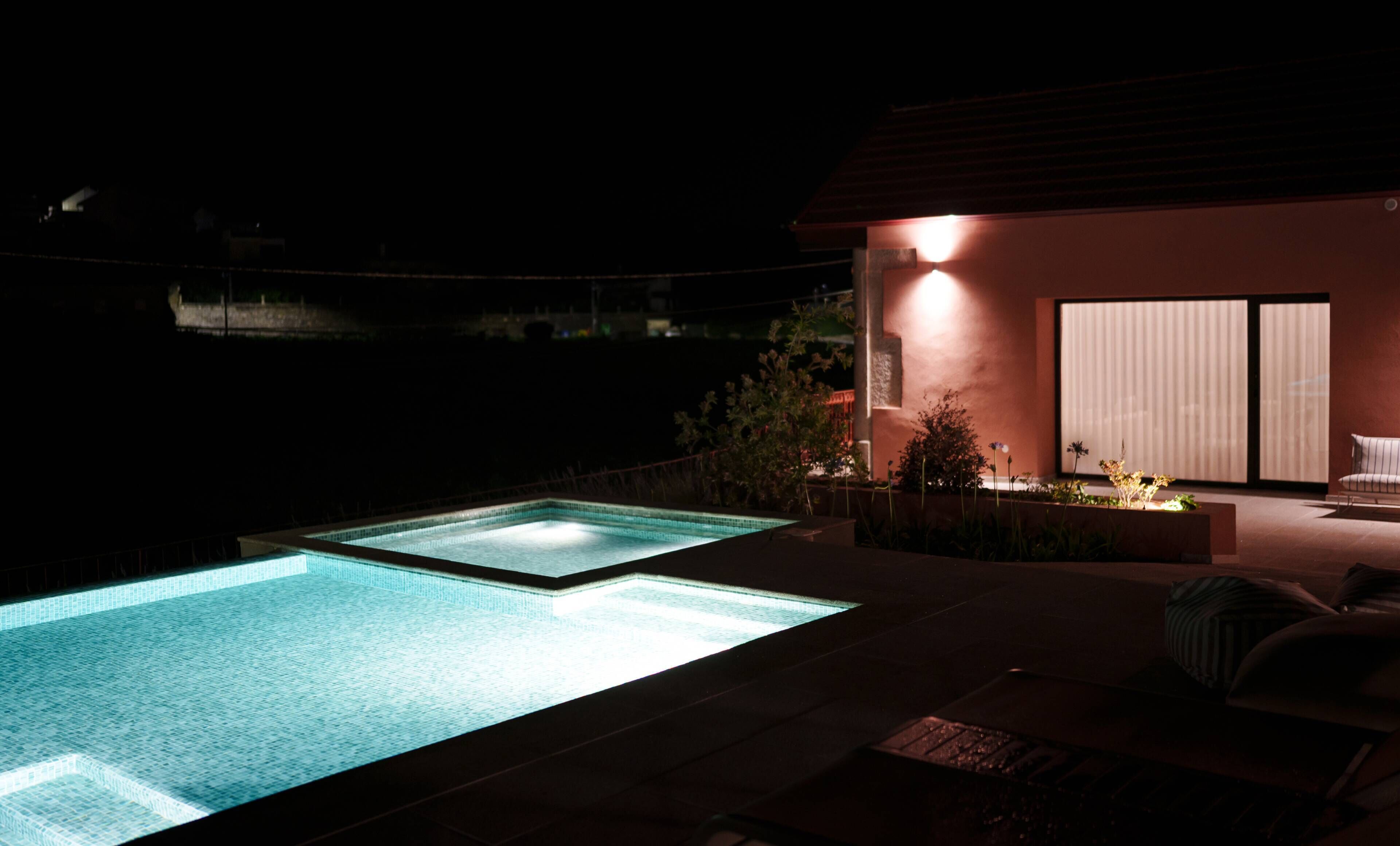A swimming pool at night with a patio area and a building with large windows.