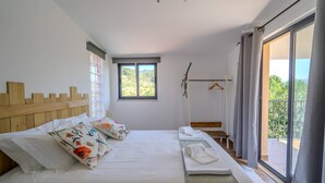 Un dormitorio con cama, almohadas, mesita de noche, ventana y balcón.