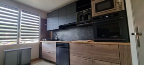 Eine Küche mit Geschirrspüler, Backofen, Mikrowelle und einem Fenster mit Jalousien.