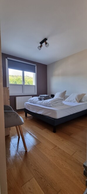 Ein Schlafzimmer mit Bett, Fenster mit Jalousien, Heizkörper und Stuhl.