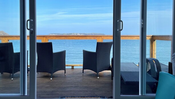 Une terrasse dotée de chaises et d’une table en osier, offrant une vue sur une étendue d’eau et une terre lointaine.
