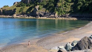 Une plage avec une eau claire, un rivage rocheux et une personne qui se promène.