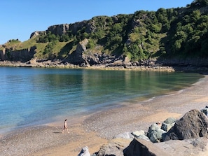 Ein Strand mit klarem Wasser, felsigem Ufer und einer Person, die spazieren geht.