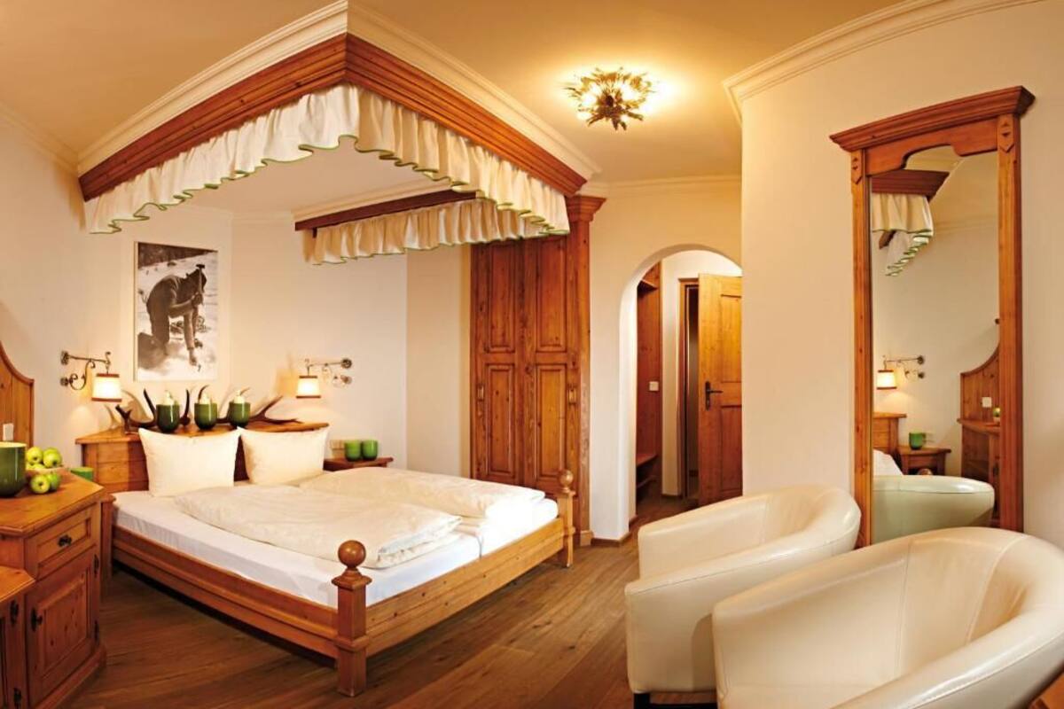 Een slaapkamer met een houten bed, een zithoek met stoelen, een spiegel en een houten garderobe.