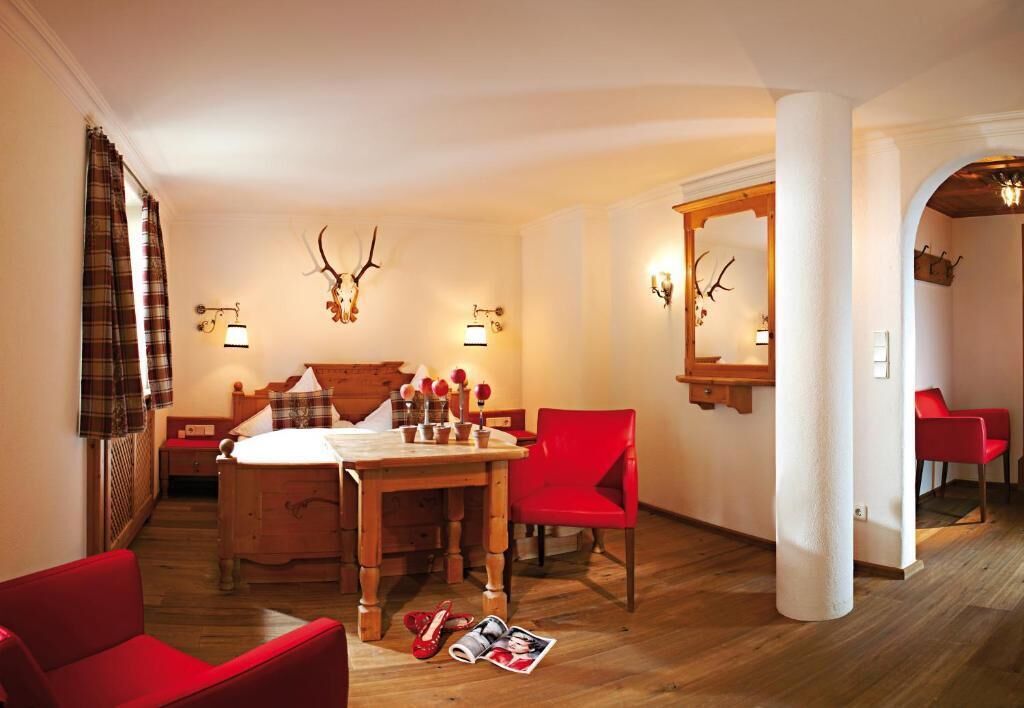 Ein Zimmer mit einem hölzernen Bett, einem Esstisch, roten Stühlen, einem Spiegel und Geweih-Dekorationen.