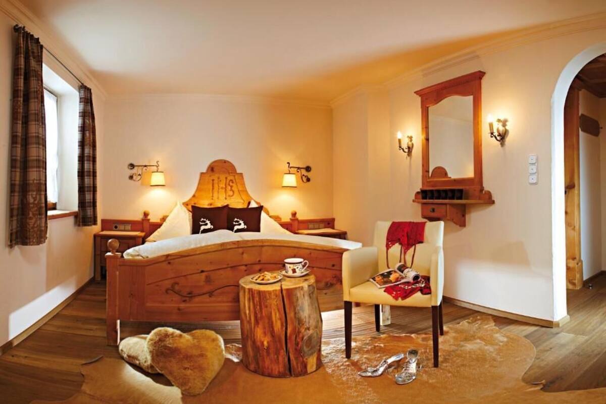 Een slaapkamer met een houten bed, twee nachtkastjes, een stoel, een spiegel en een kleden van runderhuid.