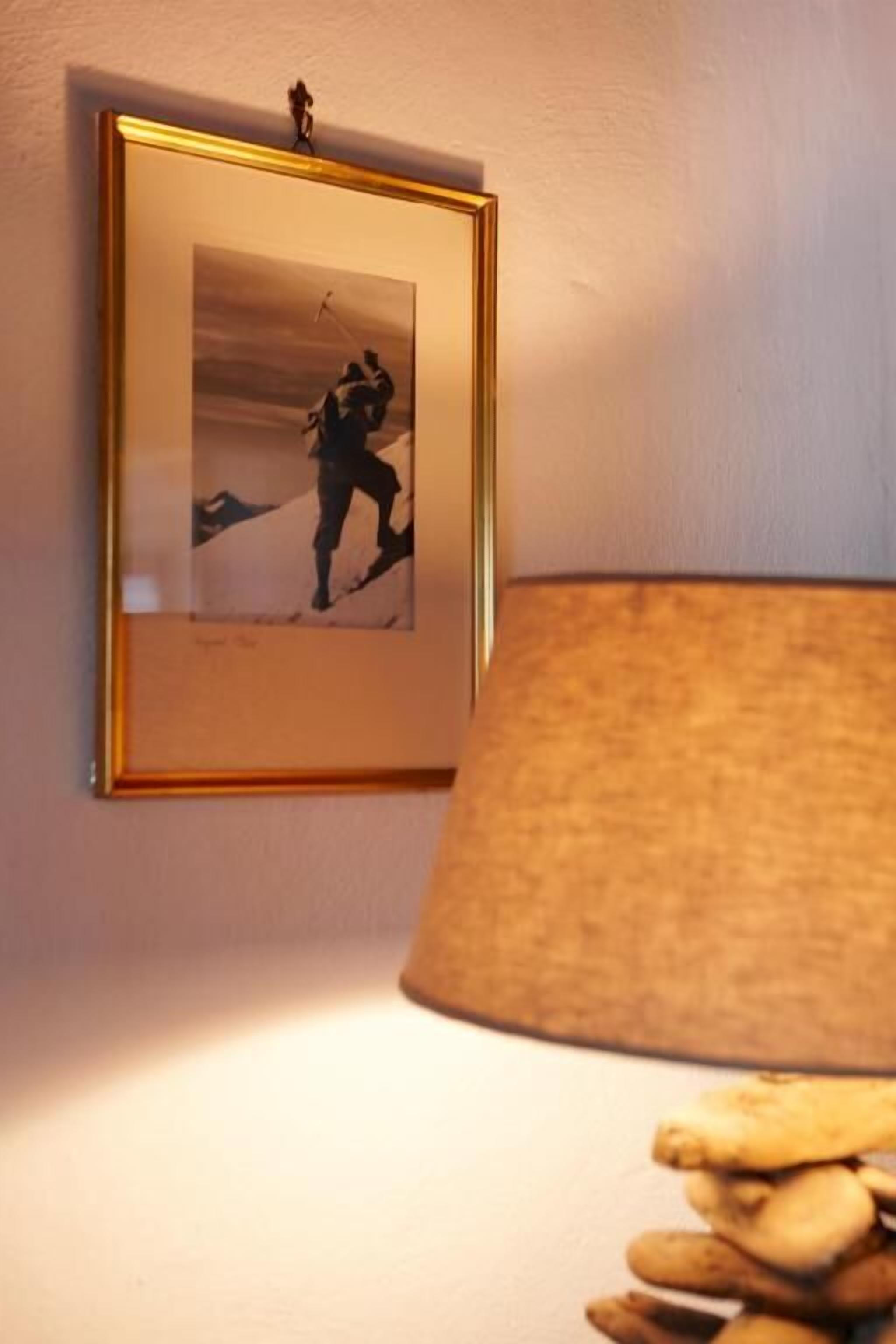 A framed picture on a wall, a lamp with a beige shade, and a stack of books or magazines.