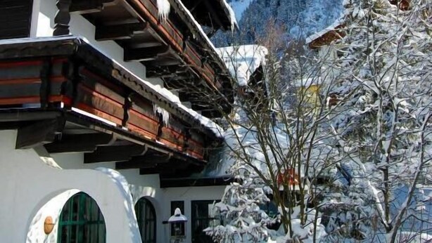 Un chalet traditionnel avec un toit en pente, des balcons en bois et une vue sur une montagne enneigée.
