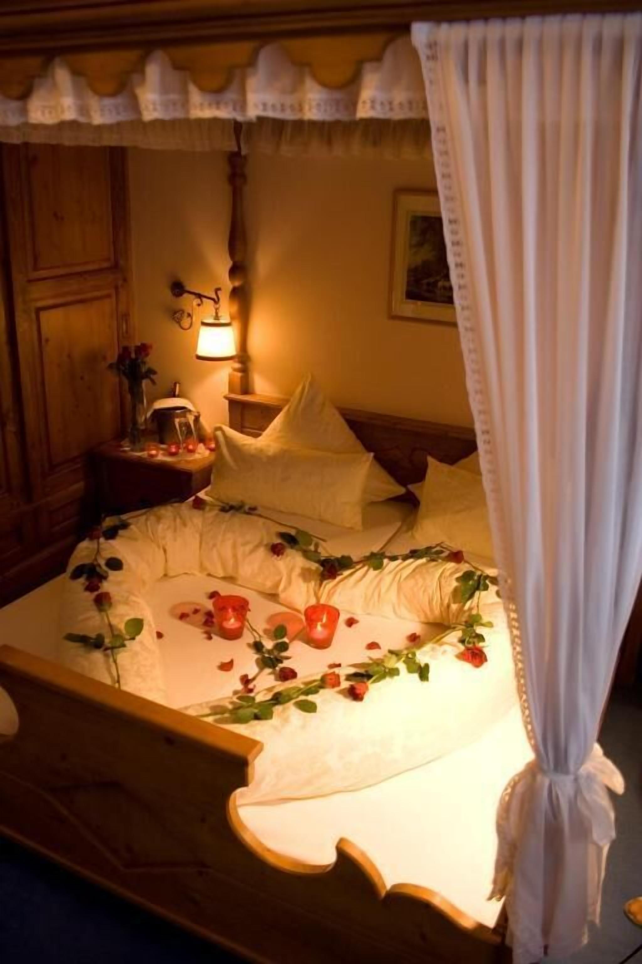 A bed with a canopy, a bedside lamp, and a nightstand with a vase of flowers.