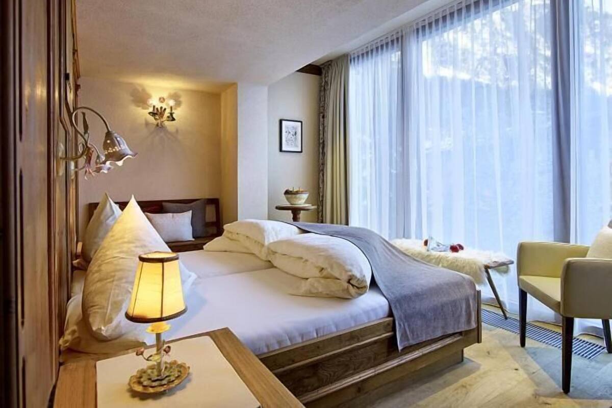 Een hotelkamer met een bed, bedlamp, stoel en grote ramen met dunne gordijnen.