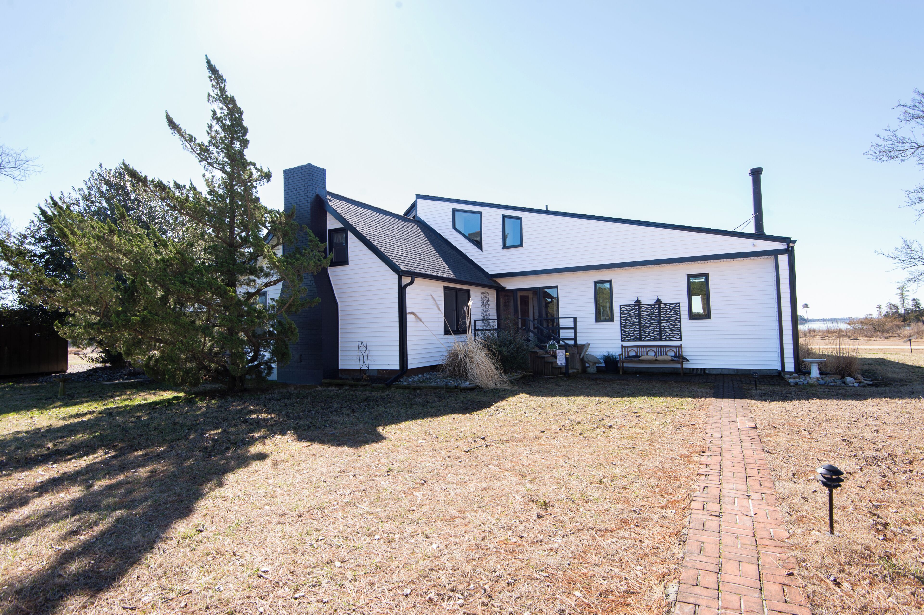 A single-story house with a brick pathway leading to the front door, a small porch with a bench, and a chimney.