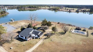 Vue aérienne d’une propriété comprenant un grand lac, une maison avec une terrasse et une piscine délimitée par une clôture.