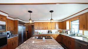 Une cuisine dotée de meubles en bois, de plans de travail en granit, d’appareils électroménagers en acier inoxydable et de luminaires suspendus.