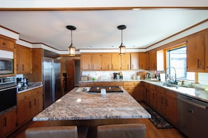 A kitchen with wooden cabinets, granite countertops, stainless steel appliances, and pendant lighting.