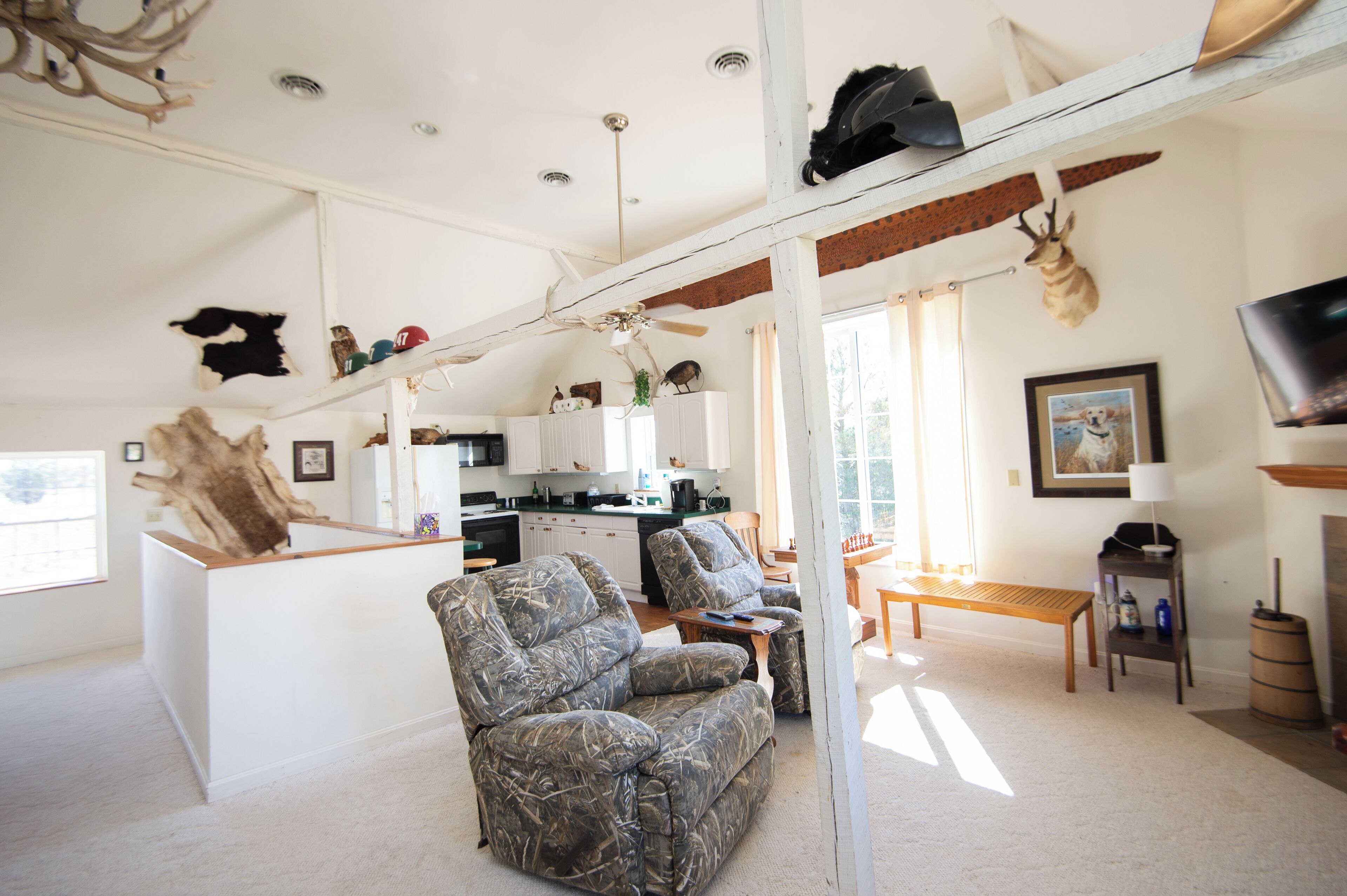 A living room with a couch, a coffee table, and a television. There is a kitchen area with cabinets and a refrigerator.
