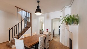 A dining area with a wooden table, chairs, a staircase, and a fireplace.
