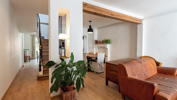 A spacious living room with a wooden staircase, a leather sofa, a dining area, and a large potted plant.