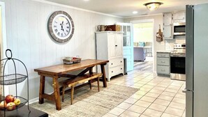 Une cuisine avec une table en bois, des placards blancs et une horloge au mur.