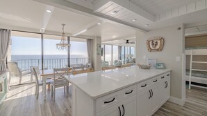 Un'ampia cucina con una grande isola, un'area pranzo vista oceano e un balcone con vista sul mare.
