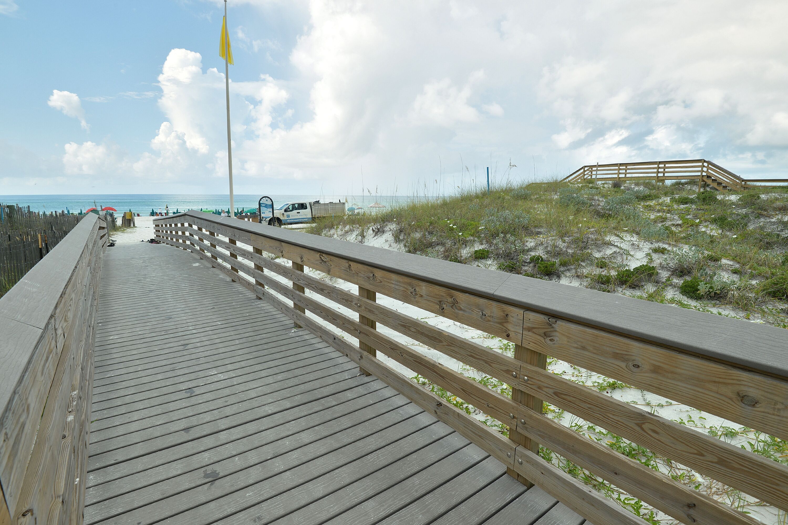 A wooden boardwalk leading to a sandy beach with a grassy dune area.